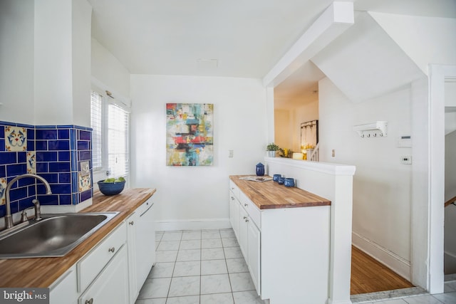 kitchen with a sink, baseboards, wooden counters, and white cabinetry