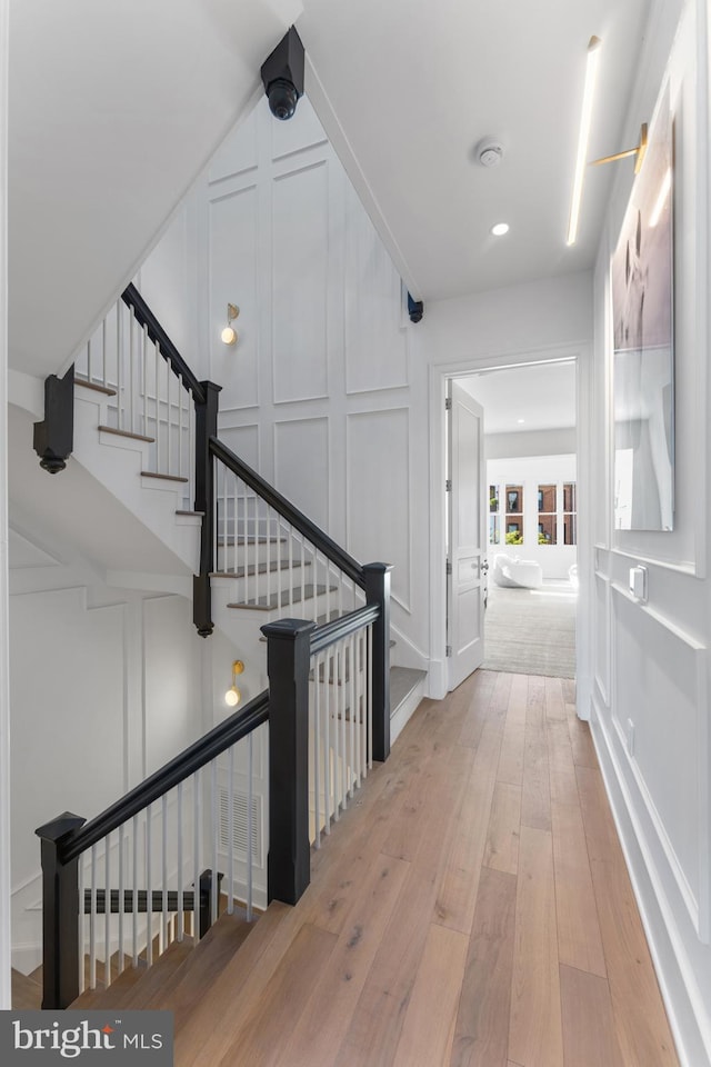 hall featuring stairway, wood-type flooring, a decorative wall, and recessed lighting