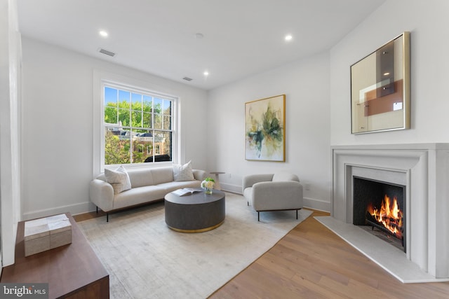 living room with visible vents, wood finished floors, baseboards, a warm lit fireplace, and recessed lighting