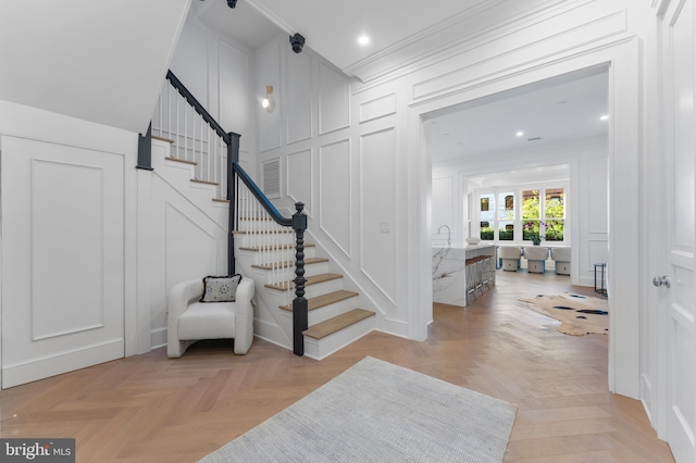 entryway with crown molding, stairs, and a decorative wall