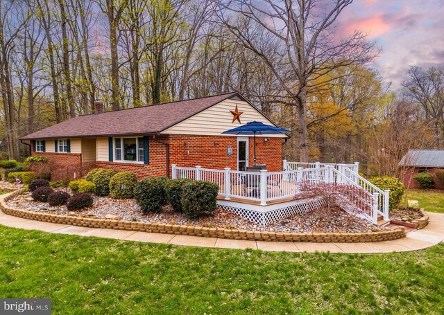 single story home with brick siding, a wooden deck, a front lawn, a chimney, and roof with shingles