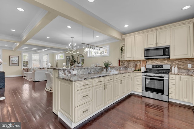 kitchen with a peninsula, appliances with stainless steel finishes, beam ceiling, open floor plan, and cream cabinetry