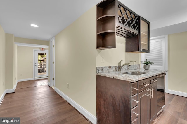 kitchen featuring light stone counters, a sink, dark brown cabinetry, baseboards, and dark wood finished floors