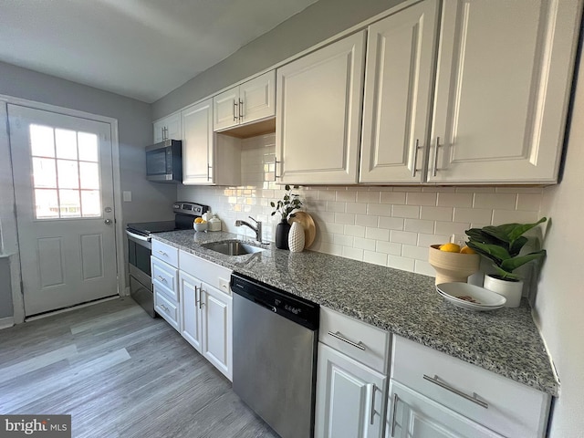kitchen with white cabinets, stainless steel appliances, light wood finished floors, a sink, and decorative backsplash