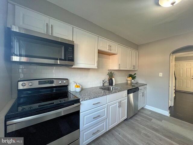 kitchen with a sink, arched walkways, light stone countertops, appliances with stainless steel finishes, and white cabinetry
