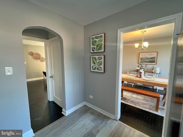 corridor featuring arched walkways, a notable chandelier, wood finished floors, and baseboards