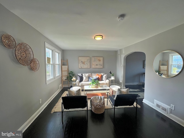 living area with baseboards, visible vents, arched walkways, and dark wood-style floors