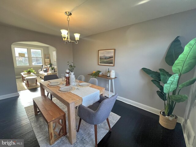 dining room with arched walkways, dark wood-type flooring, and baseboards