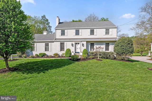 view of front of home with a chimney, a shingled roof, and a front yard