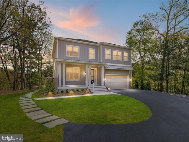 traditional home with an attached garage, board and batten siding, a standing seam roof, a yard, and driveway