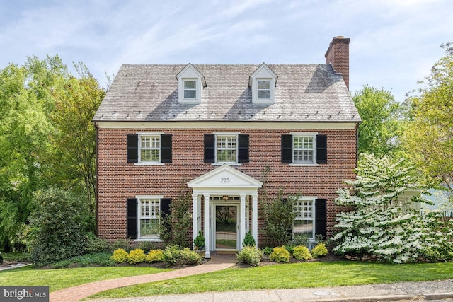 georgian-style home with brick siding, a high end roof, a chimney, and a front yard