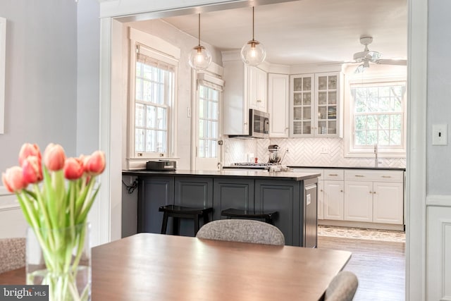 kitchen with white cabinets, dark countertops, a breakfast bar, stainless steel microwave, and glass insert cabinets