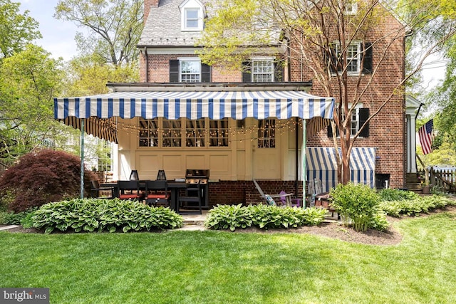 rear view of house featuring brick siding, a lawn, a chimney, and a patio