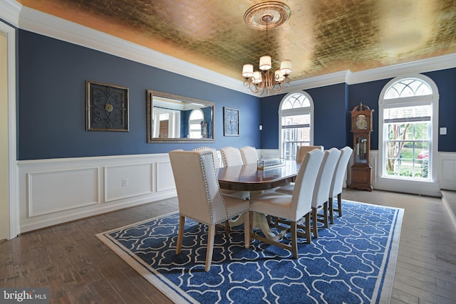 dining area featuring a healthy amount of sunlight, crown molding, a wainscoted wall, a notable chandelier, and hardwood / wood-style floors