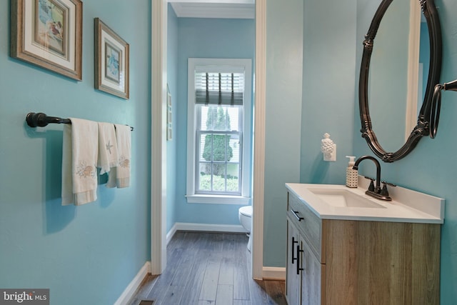 half bath featuring vanity, baseboards, wood finished floors, and toilet