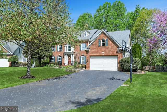 colonial-style house featuring brick siding, a garage, a front yard, and aphalt driveway