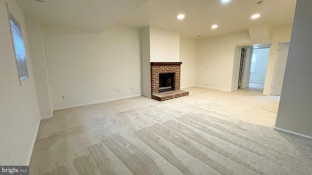 unfurnished living room featuring light colored carpet, a brick fireplace, recessed lighting, and baseboards