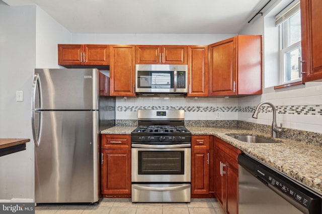 kitchen featuring light tile patterned floors, decorative backsplash, a sink, appliances with stainless steel finishes, and light stone countertops