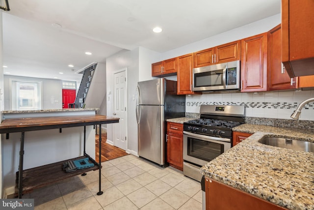 kitchen with tasteful backsplash, stainless steel appliances, light stone countertops, and a sink