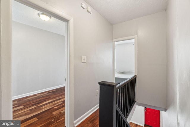 hallway featuring an upstairs landing, baseboards, wood finished floors, and a textured ceiling