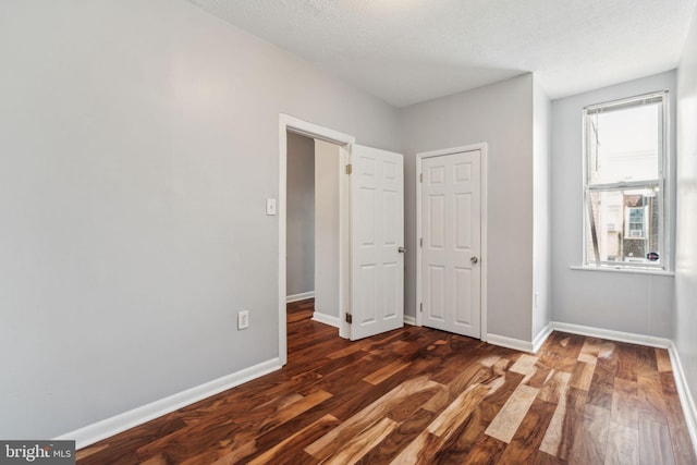 unfurnished bedroom with a textured ceiling, wood finished floors, and baseboards