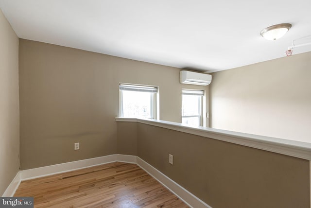 spare room with light wood-type flooring, a wall mounted air conditioner, and baseboards