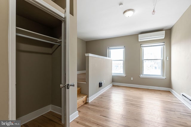 interior space with an AC wall unit, baseboards, multiple windows, and light wood-style flooring