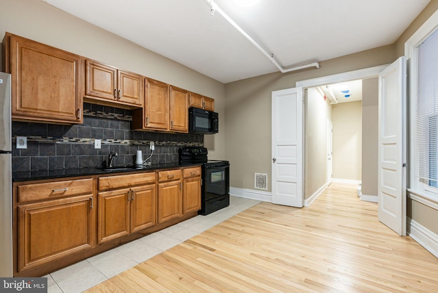 kitchen with visible vents, brown cabinetry, a sink, backsplash, and black appliances