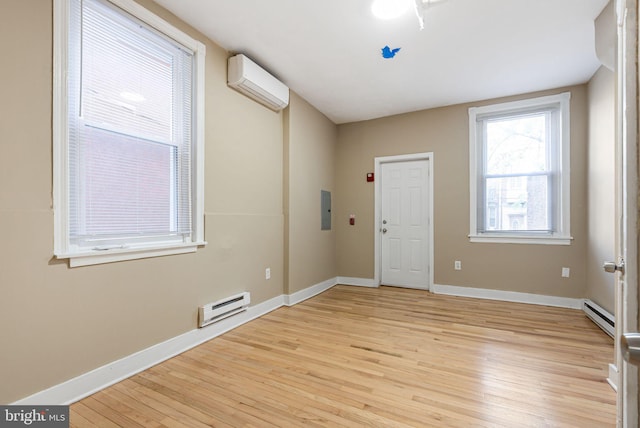 spare room featuring a wall mounted air conditioner, light wood-style flooring, electric panel, and baseboard heating