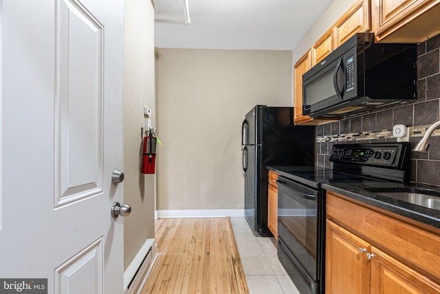 kitchen with decorative backsplash, baseboard heating, a sink, black appliances, and dark stone counters