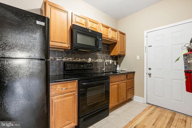 kitchen featuring dark countertops, a sink, decorative backsplash, light wood-type flooring, and black appliances