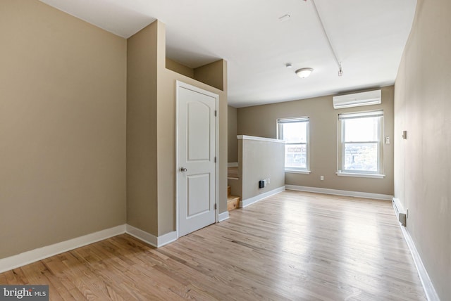 unfurnished room featuring baseboard heating, baseboards, a wall unit AC, and light wood-style flooring
