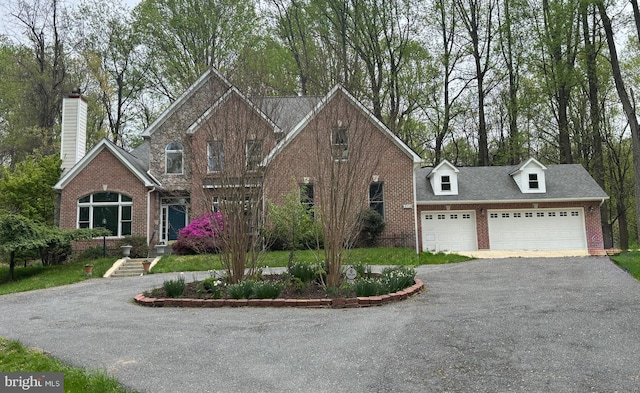 traditional home with a chimney, aphalt driveway, brick siding, and a garage