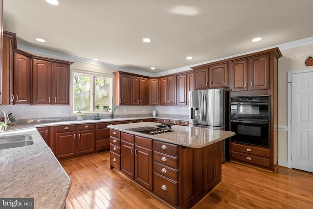 kitchen featuring light wood-style flooring, black appliances, crown molding, and a sink