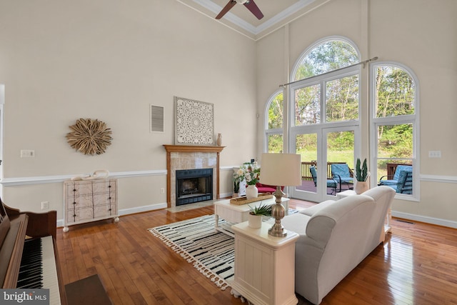 living area with a tile fireplace, visible vents, a ceiling fan, crown molding, and a towering ceiling