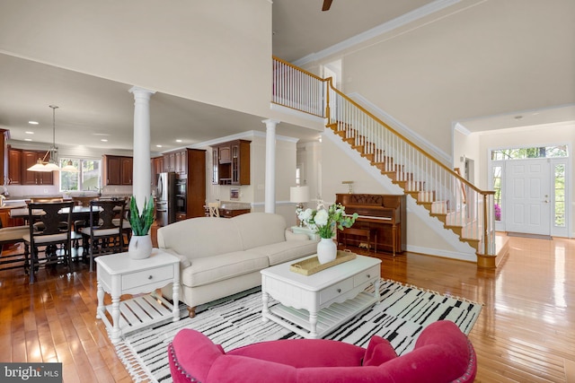 living area with ornamental molding, light wood finished floors, stairs, and decorative columns