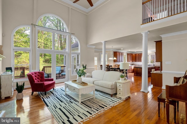living area with light wood-style floors, decorative columns, crown molding, a ceiling fan, and a towering ceiling