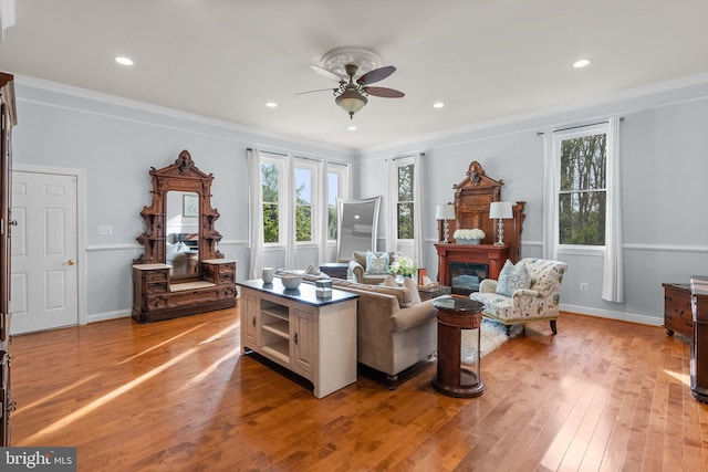 living room with ornamental molding, ceiling fan, light wood-style floors, and a glass covered fireplace