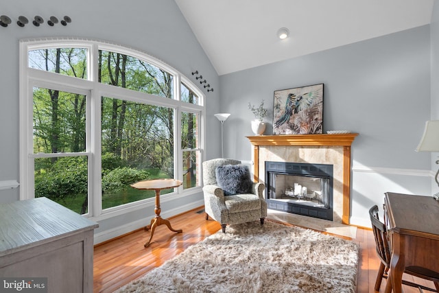 sitting room featuring wood finished floors, high vaulted ceiling, a high end fireplace, and baseboards