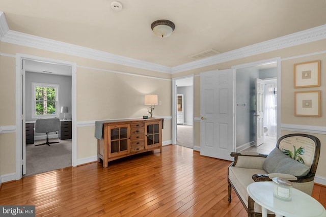 sitting room featuring baseboards, visible vents, ornamental molding, and light wood-type flooring