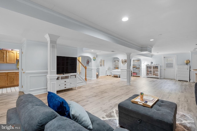 living room featuring decorative columns, arched walkways, ornamental molding, and light wood finished floors