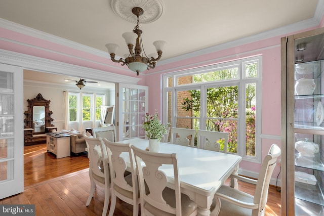 dining area with a chandelier, a healthy amount of sunlight, crown molding, and wood-type flooring