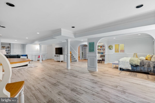 living area with a decorative wall, crown molding, built in shelves, and arched walkways