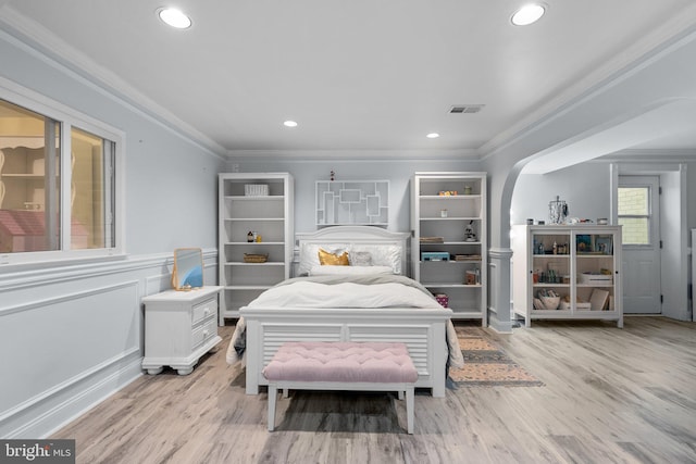bedroom with light wood finished floors, visible vents, ornamental molding, and arched walkways