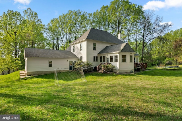 back of property featuring a lawn, a trampoline, central AC unit, and a chimney