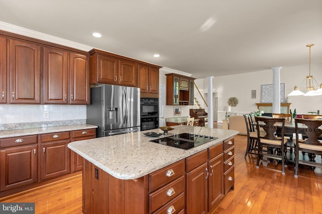 kitchen with light stone countertops, hanging light fixtures, black appliances, light wood finished floors, and ornate columns