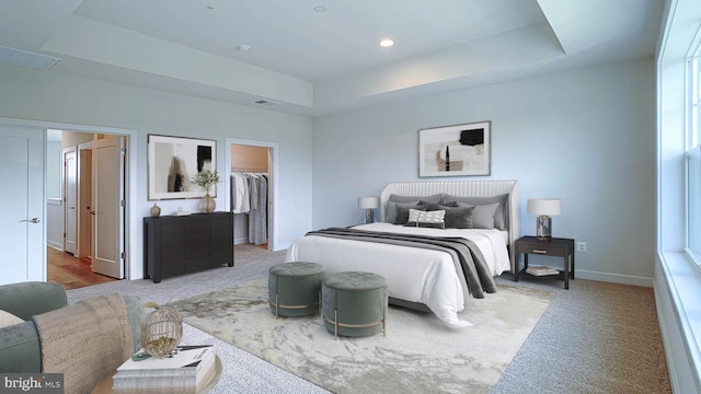 bedroom featuring a raised ceiling, carpet flooring, and a walk in closet