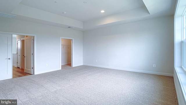 unfurnished bedroom featuring a walk in closet, carpet floors, recessed lighting, baseboards, and a tray ceiling