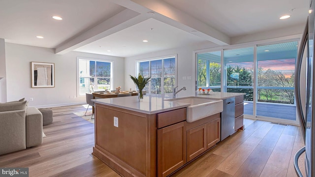 kitchen with a sink, beam ceiling, stainless steel appliances, open floor plan, and light wood-type flooring
