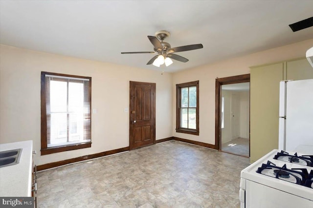 kitchen featuring a sink, baseboards, a ceiling fan, white appliances, and light countertops